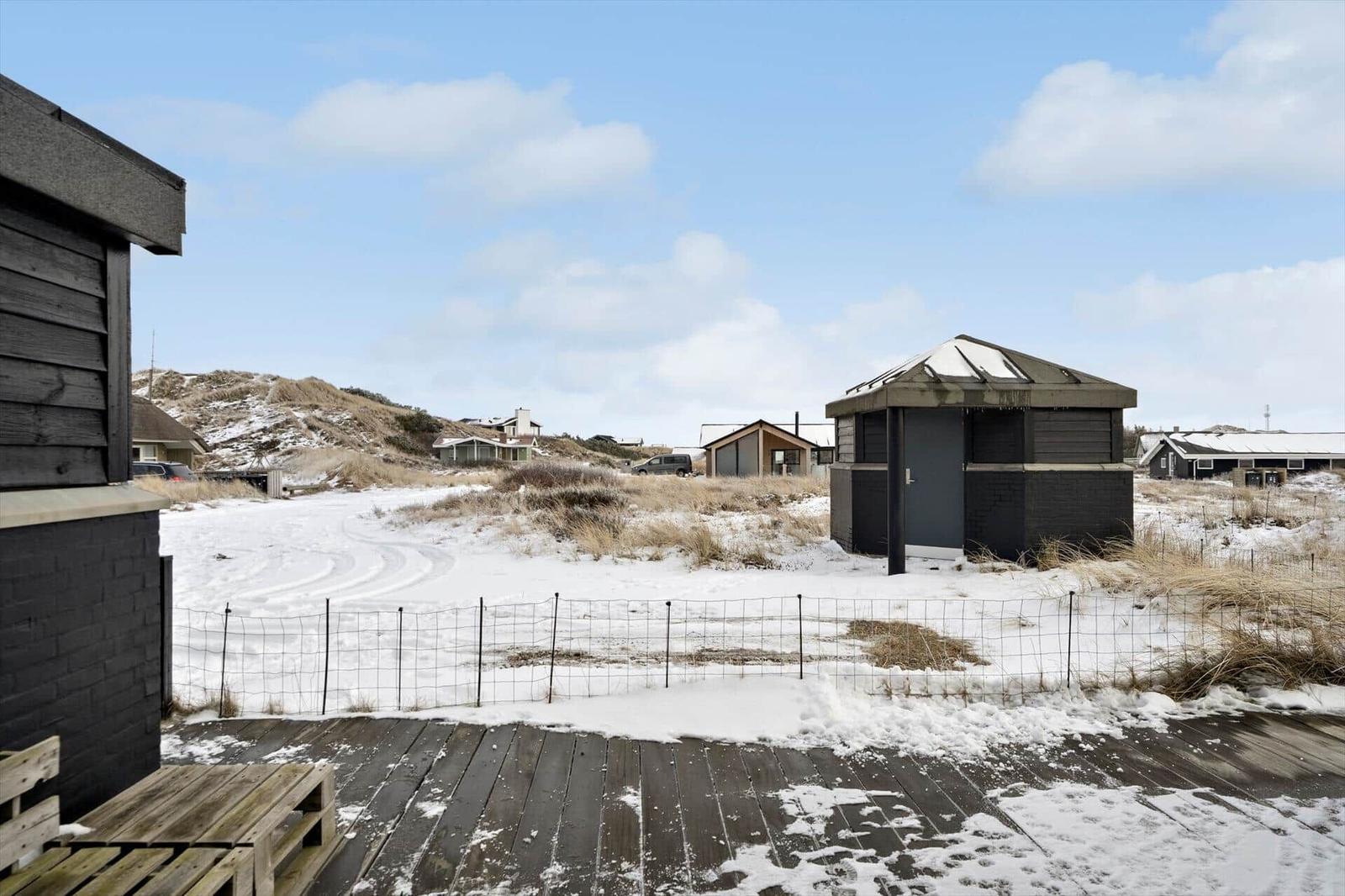 Schneebedeckter Strandbereich mit Holzterrasse und mehreren Häusern im Hintergrund.