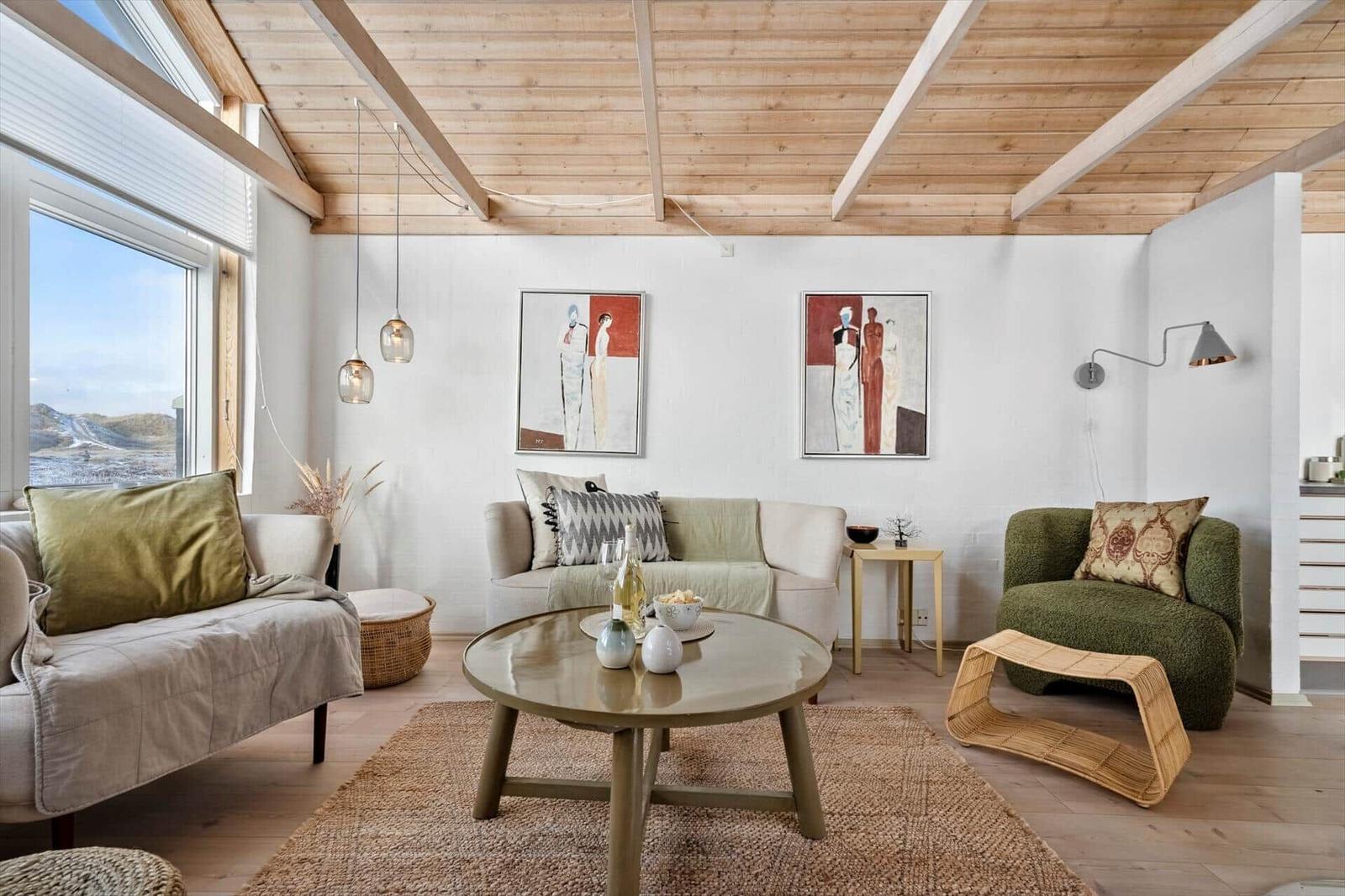 Wohnzimmer mit Sofa, Sessel und runden Tisch. Holzdecke und Fenster mit Blick.