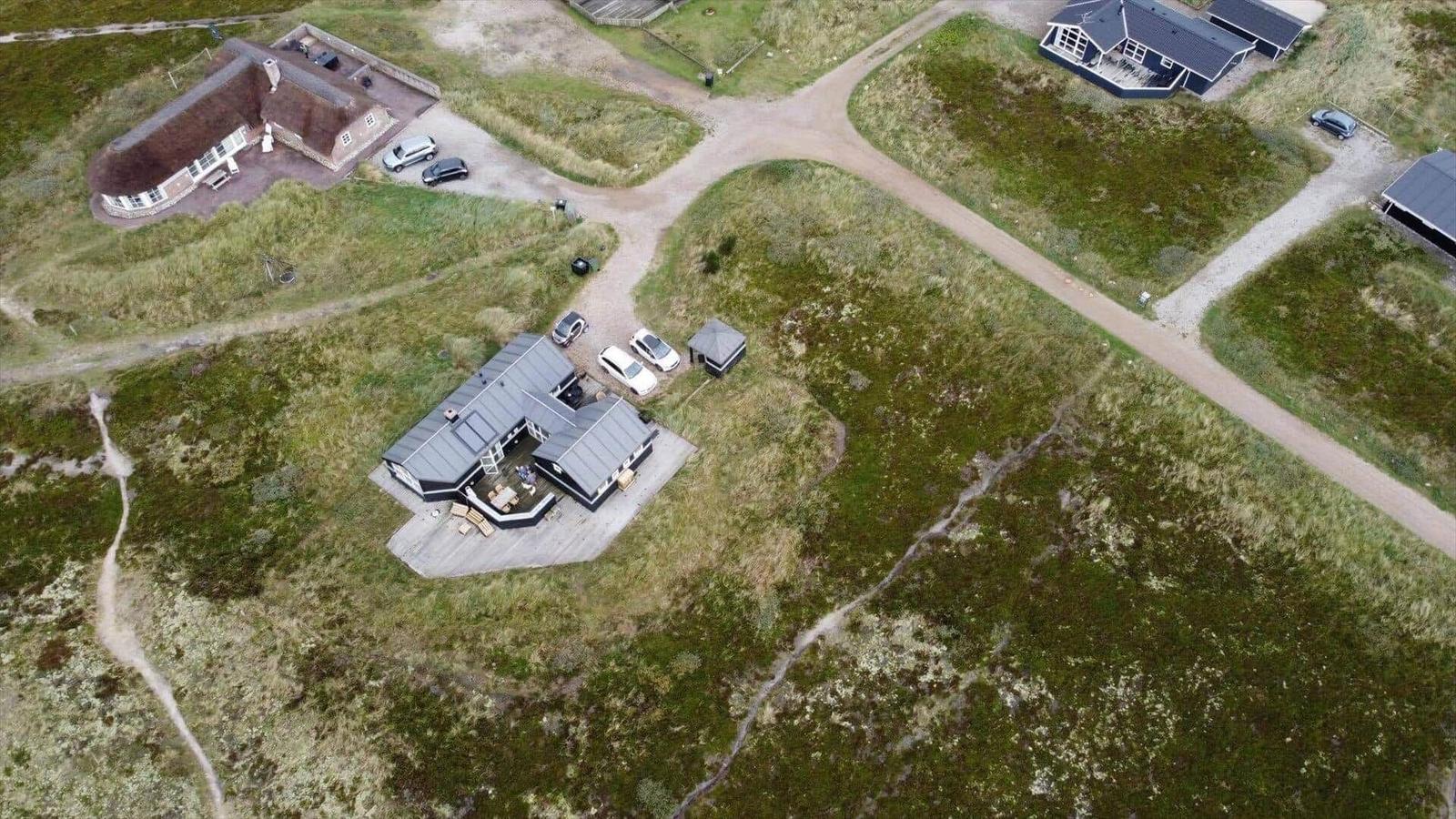 Aerial view of several houses with gravel paths and parked cars on grassy terrain.