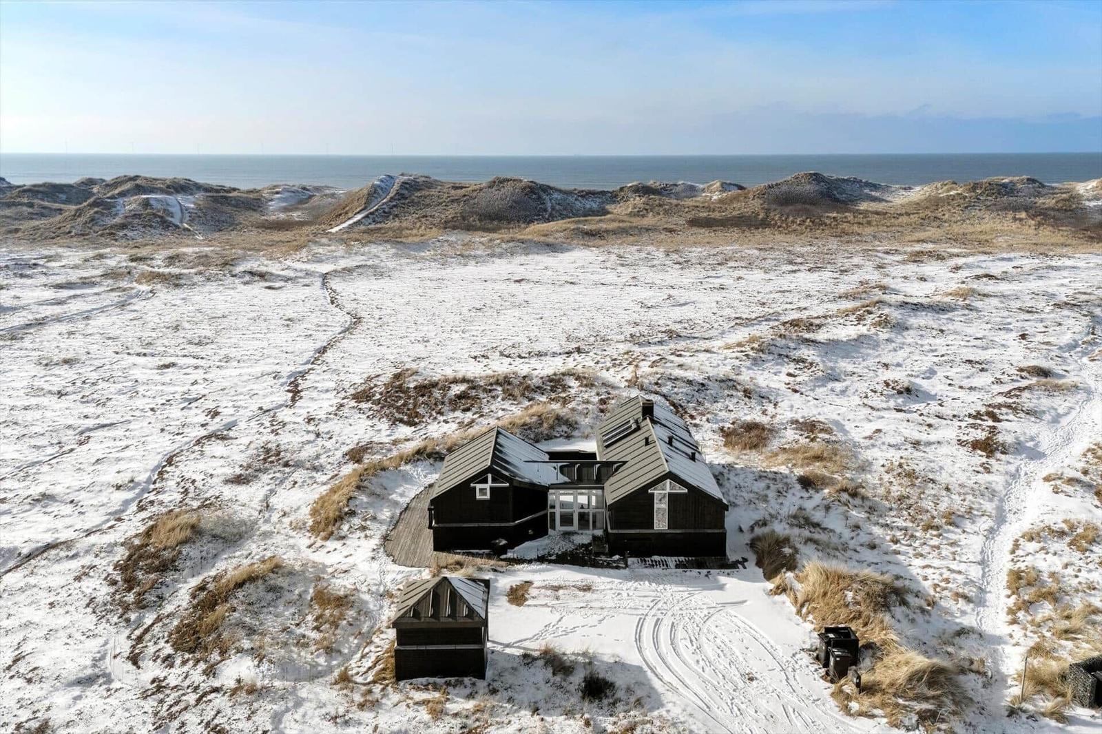 Schwarzes Haus auf schneebedeckten Dünen mit Blick auf das Meer.