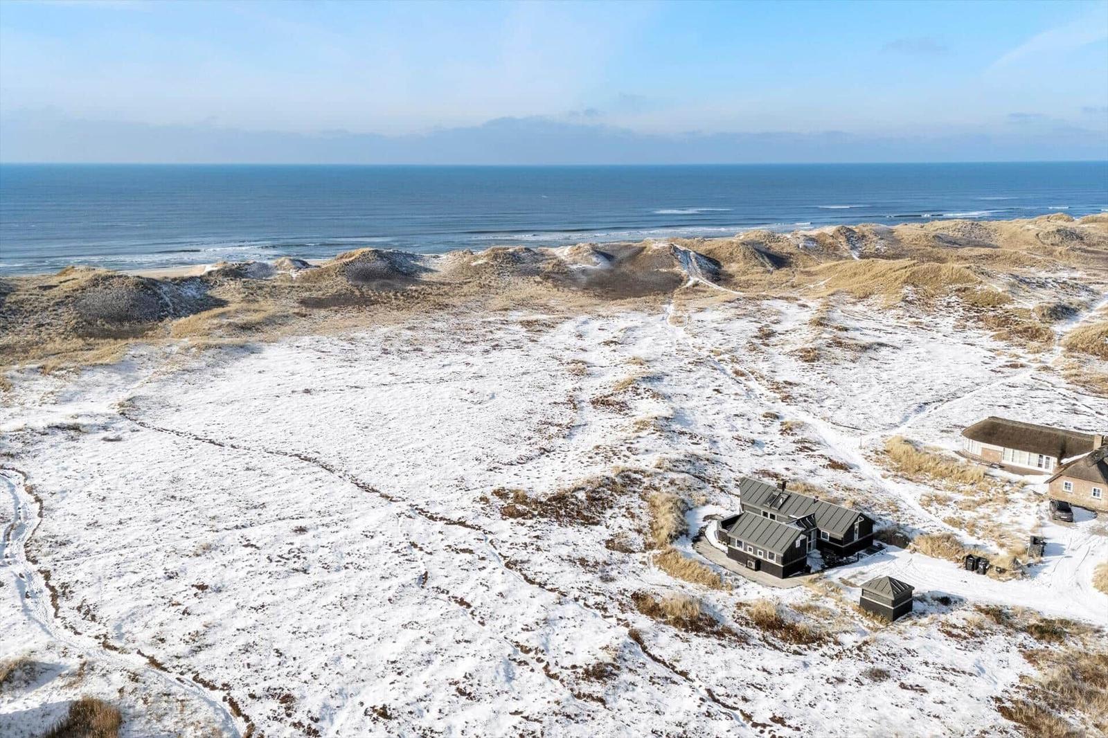 Schneebedeckte Dünenlandschaft mit Strandhaus und Blick auf das Meer.