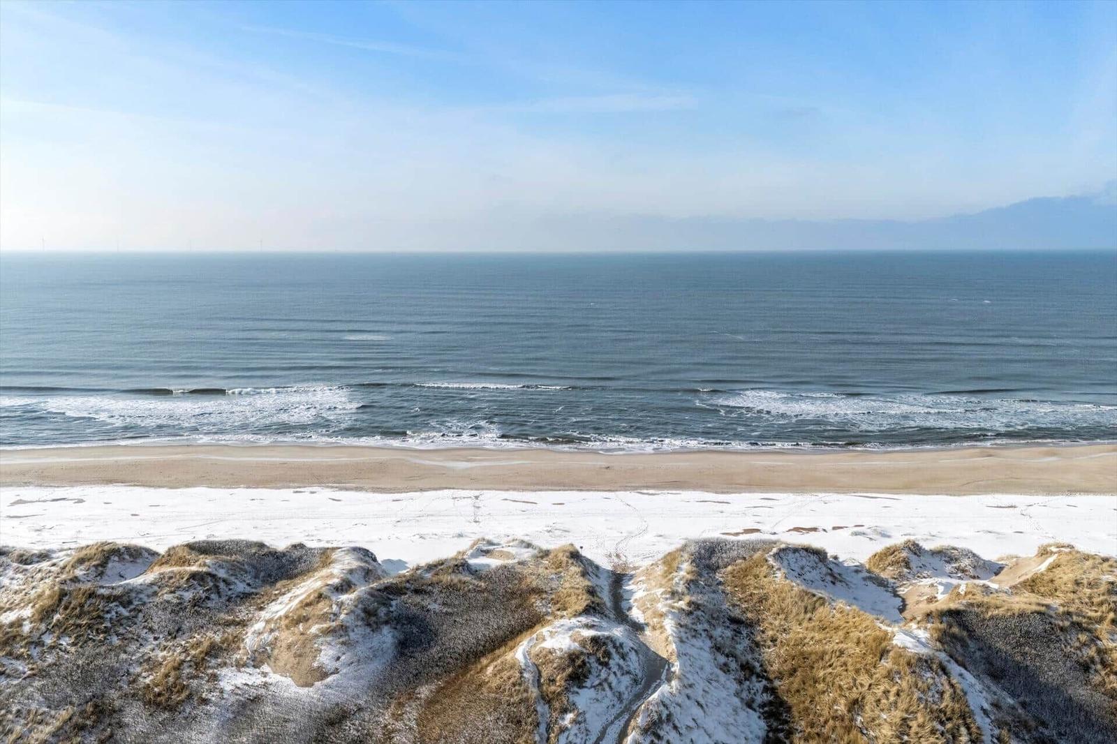 Meer und Strand mit schneebedeckten Dünen im Vordergrund.