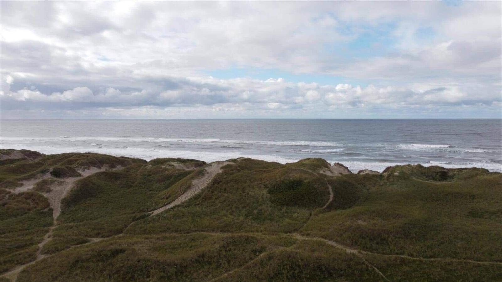 Meer mit Dünen und Wanderpfaden unter bewölktem Himmel.