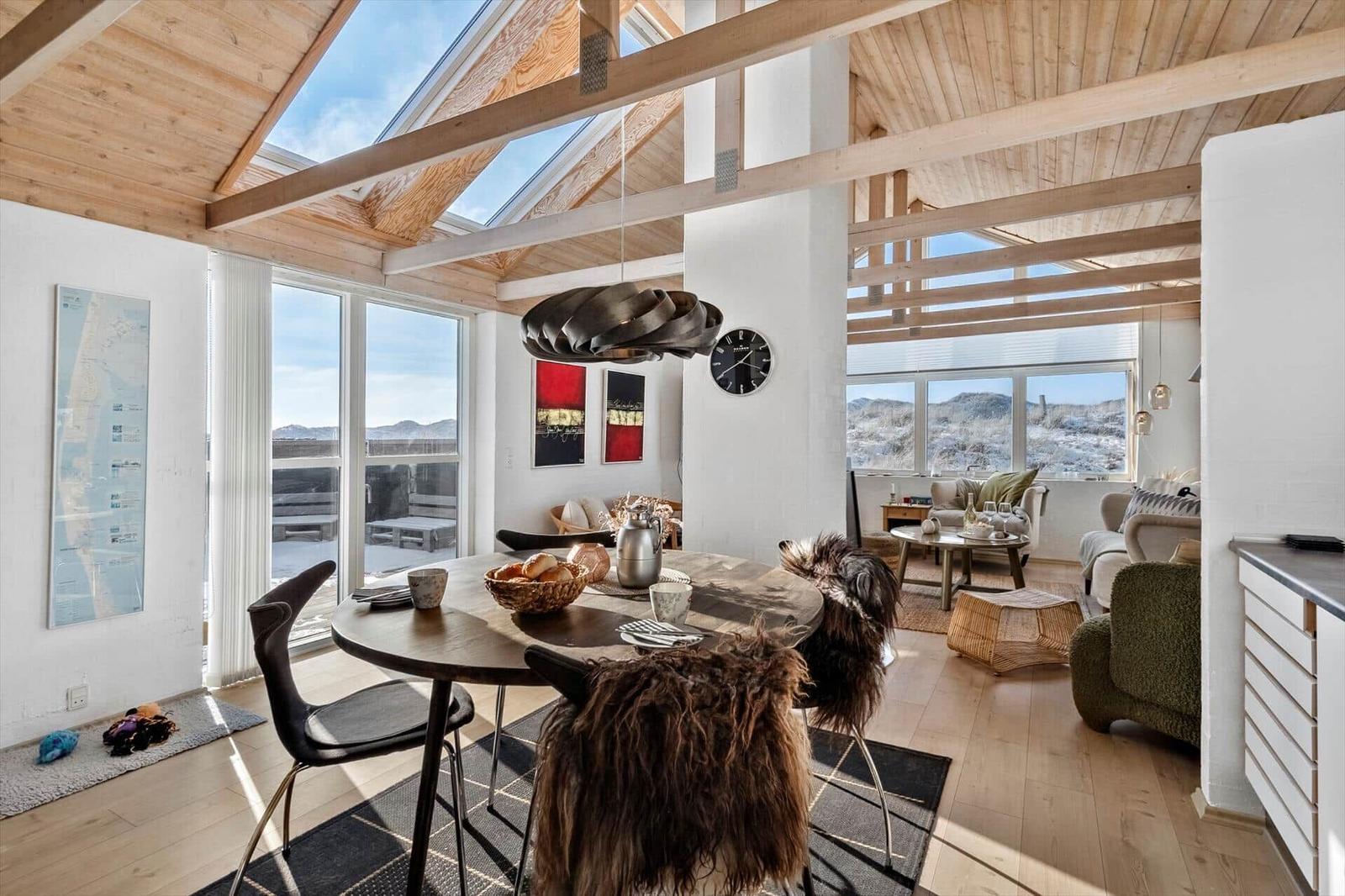 Eingangsbereich mit Essbereich und Wohnzimmer. Holzdecke, große Fenster und Möbel sind sichtbar.