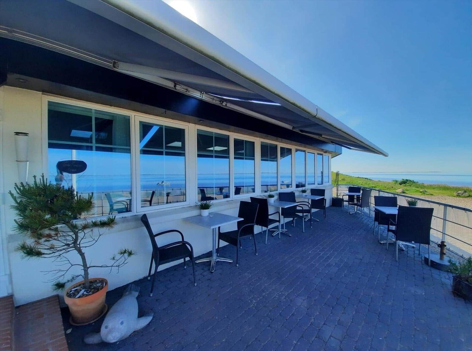 Terrace with tables and chairs, view of the sea and green landscape.