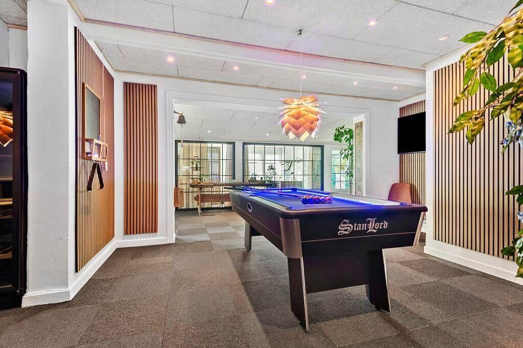 Pool table with blue felt in a room with wooden walls and ceiling light.