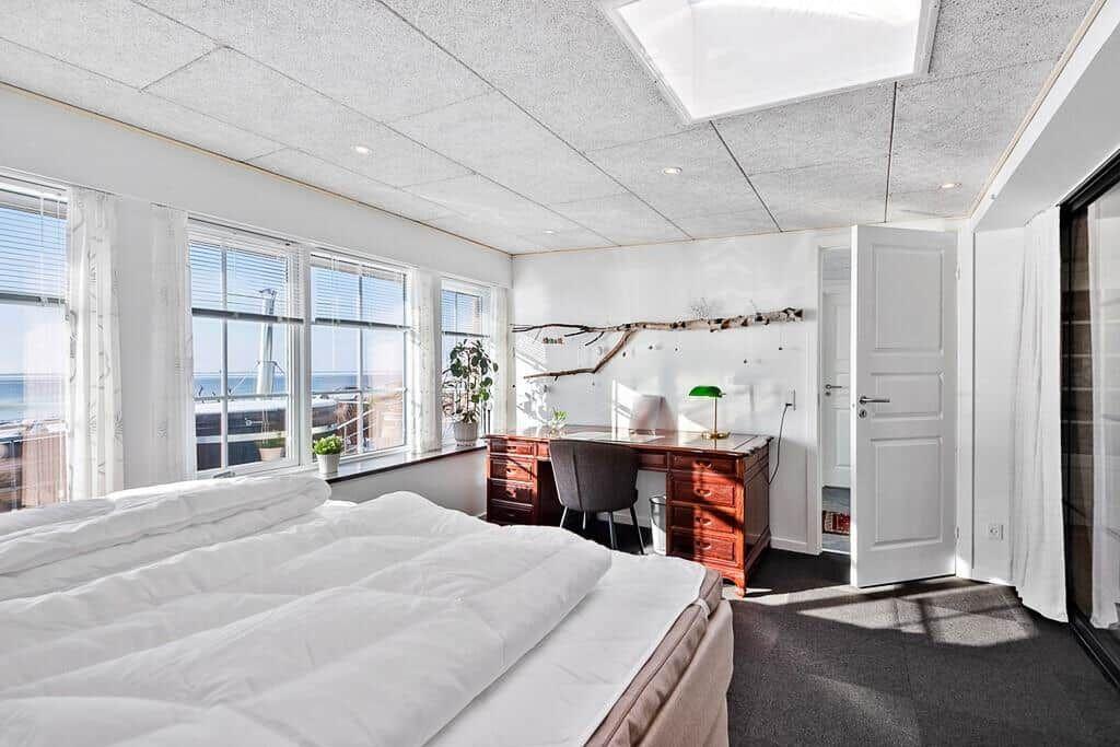 Bedroom with bed, desk, and windows overlooking the sea.
