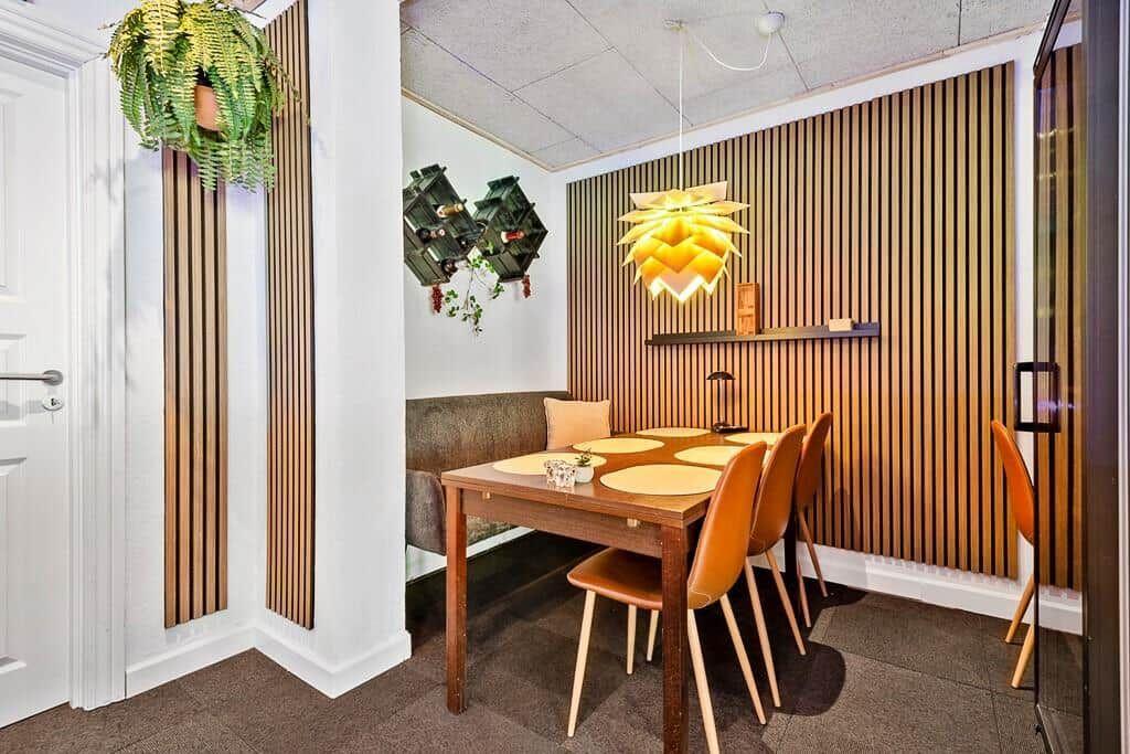 Dining room with wooden wall, table, chairs, plants, and hanging lamp.