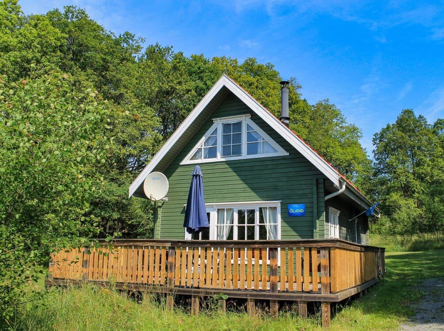 Grünes Holzhaus mit Balkon und Satellitenantenne in Waldnähe