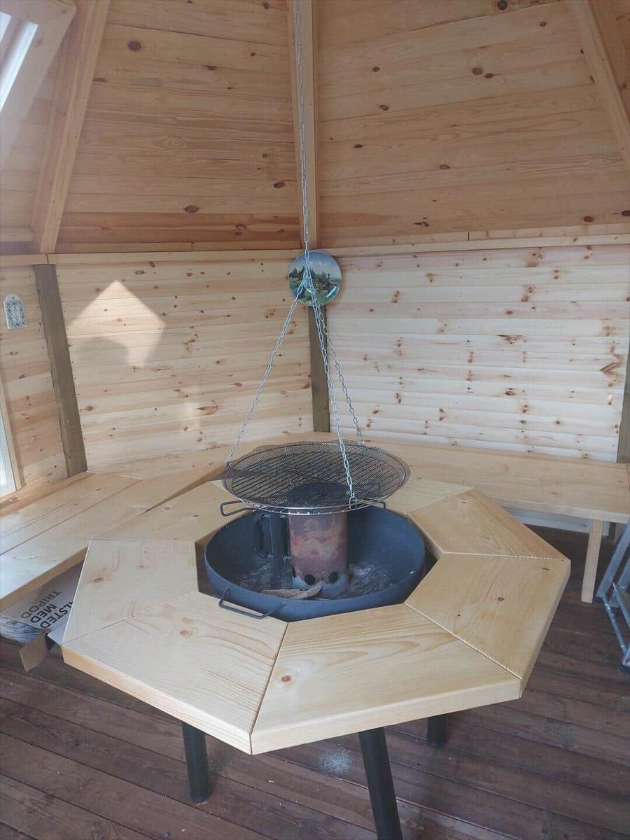 Wood sauna with hanging grill and benches around fire pit