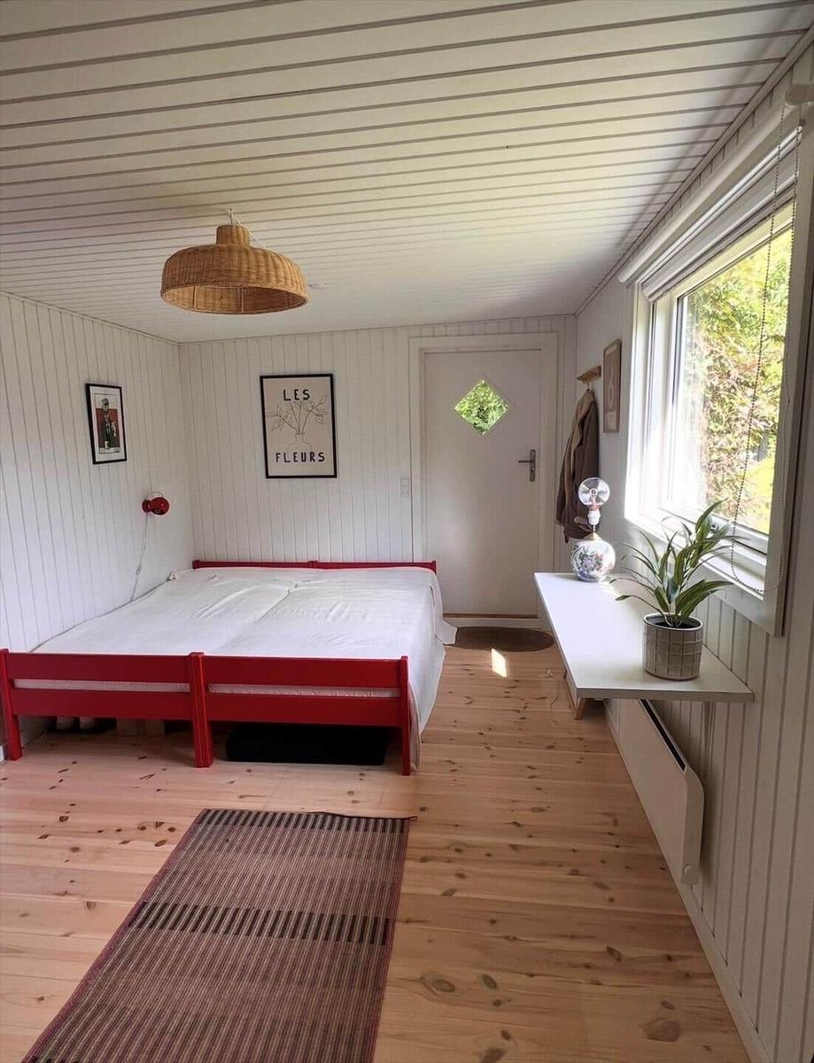 Bedroom with red bed, wooden floor, and window with plant.