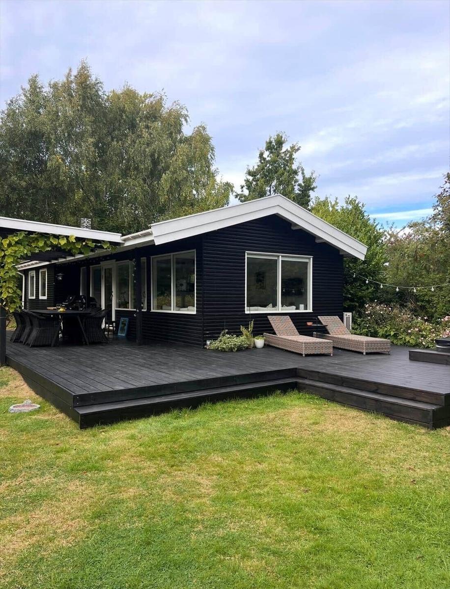 Black house with terrace, lounge chairs, and garden.
