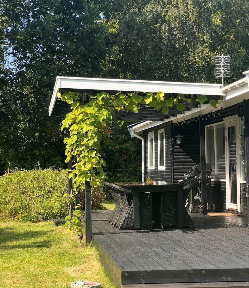 Terrace with table, chairs, and grill under a white roof. Green plants climb upward.