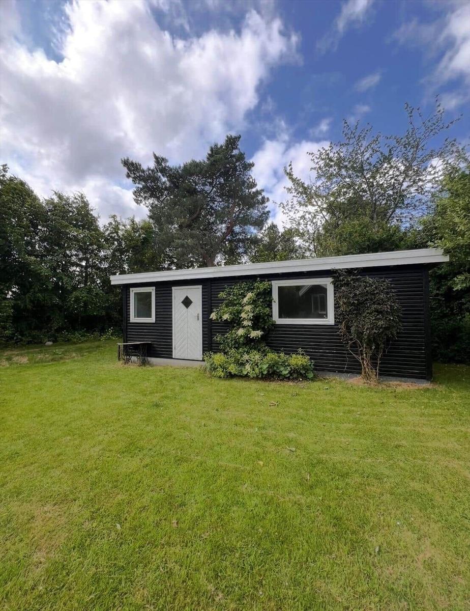 Black wooden house with white door and windows on green lawn.