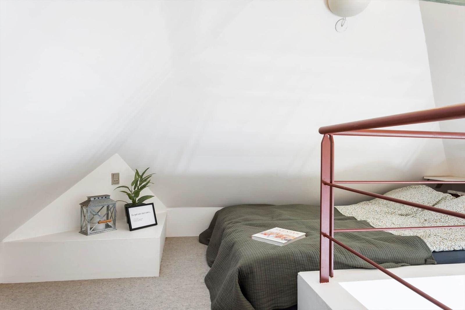 Schlafzimmer mit Dachschräge, Bett mit Metallgestell und Nachttisch mit Pflanze und Laterne.