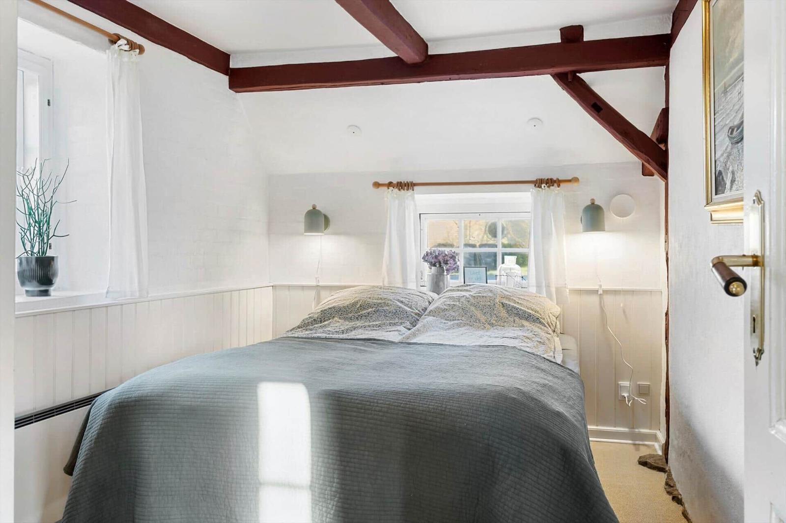 Schlafzimmer mit Bett, Fenstern und Holzbalken an der Decke.