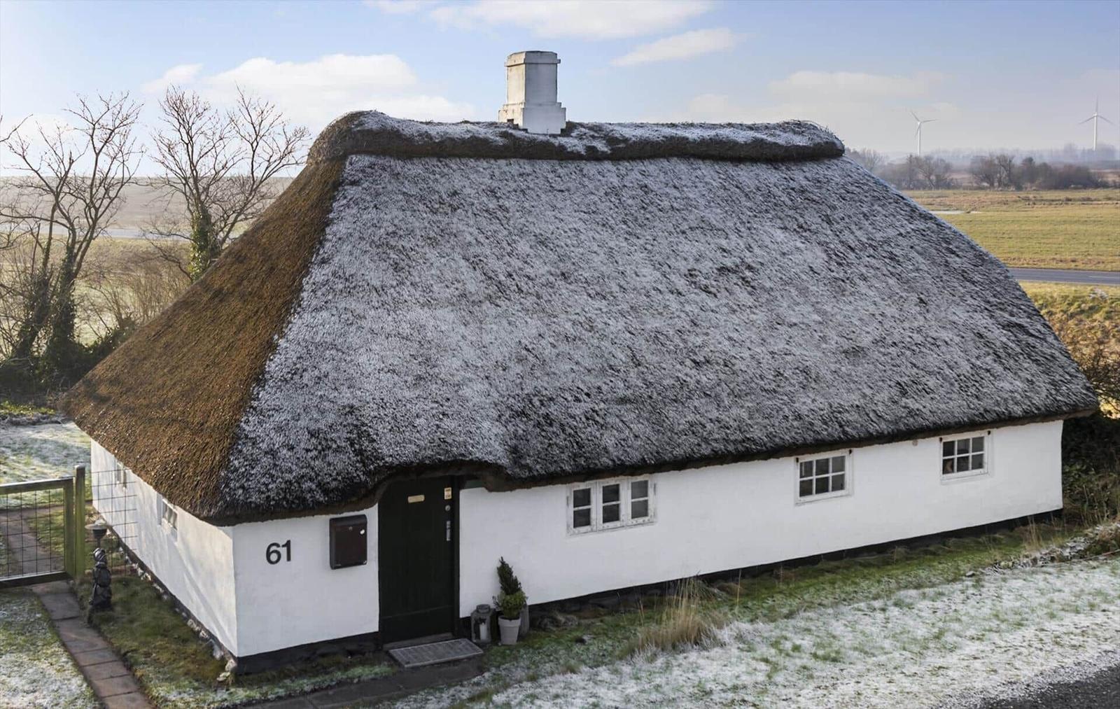 Wohnhaus mit strohgedecktem Dach und weißer Fassade. Nummer 61. Schnee bedeckt den Boden und das Dach.