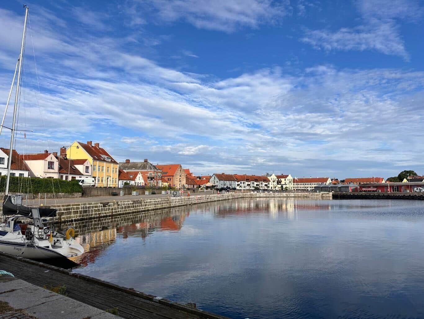 Hafen mit Segelyacht und Reflexionen von Häusern im Wasser.