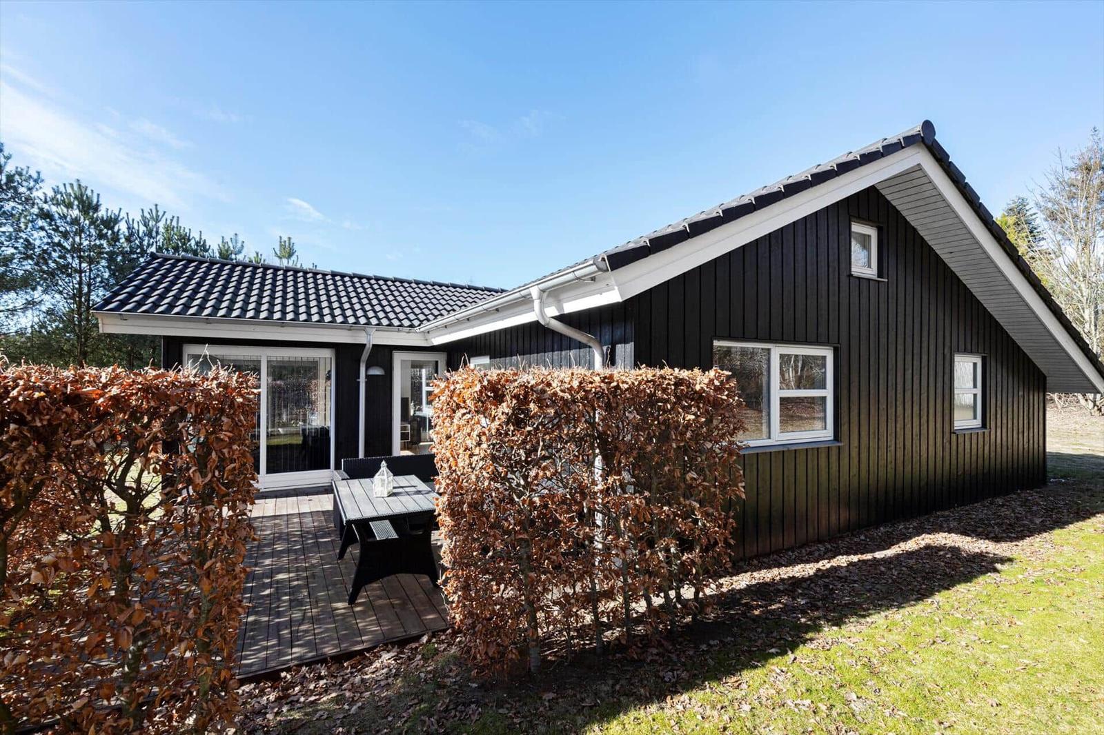 Black wooden house with terrace and garden. White windows and roof gutter.