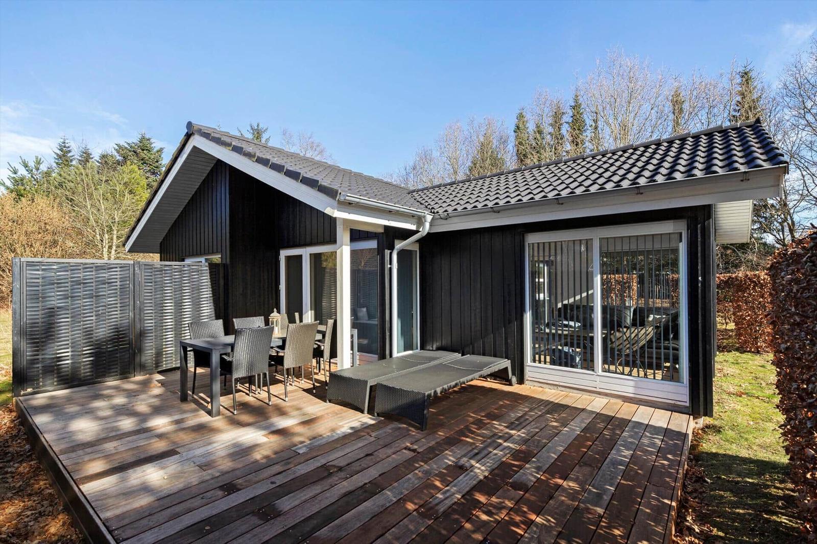 House with terrace, table, chairs, and loungers. Black facade, wooden deck, and glass front.