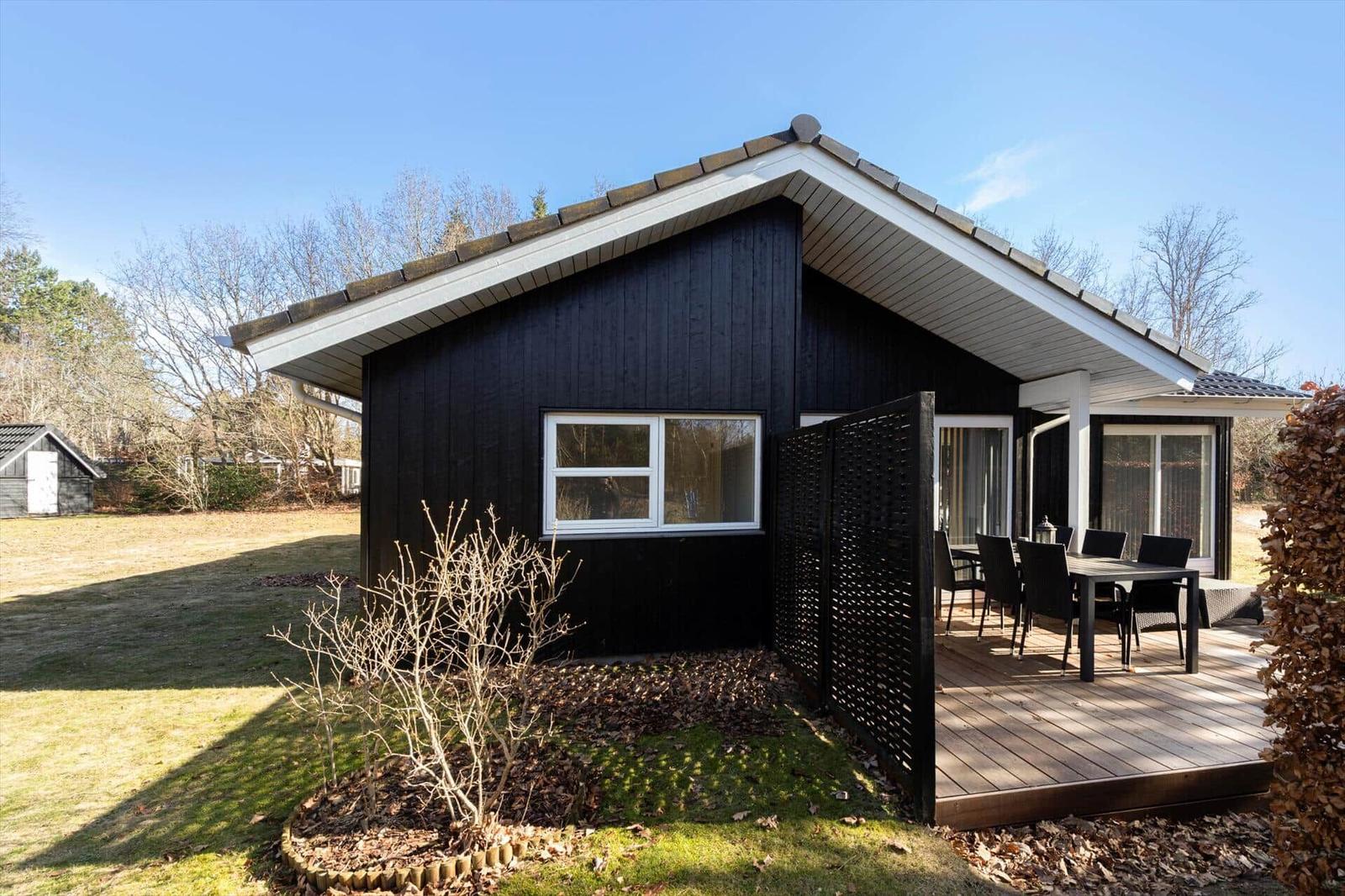 Black house with terrace and garden. Table and chairs on the veranda.