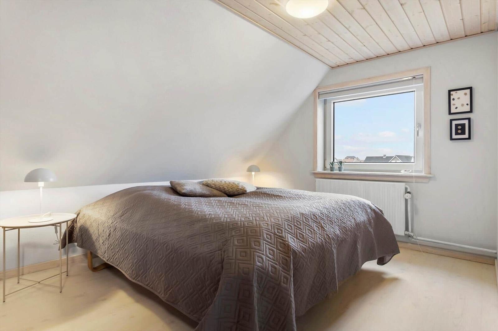 Schlafzimmer mit Bett, Fenster und Holzdecke.