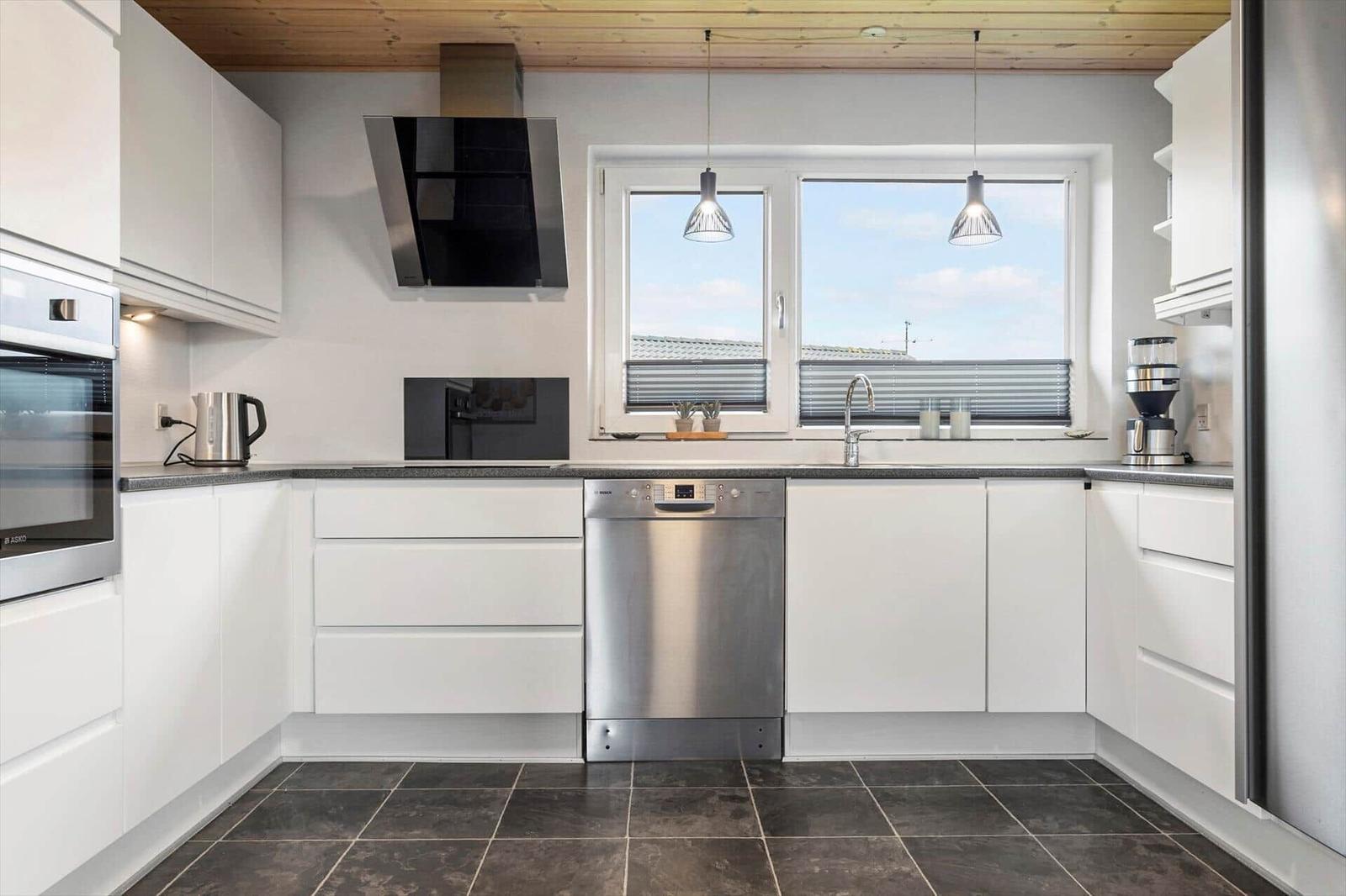 Moderne Küche mit weißen Schränken, Edelstahlgeräten und großem Fenster.