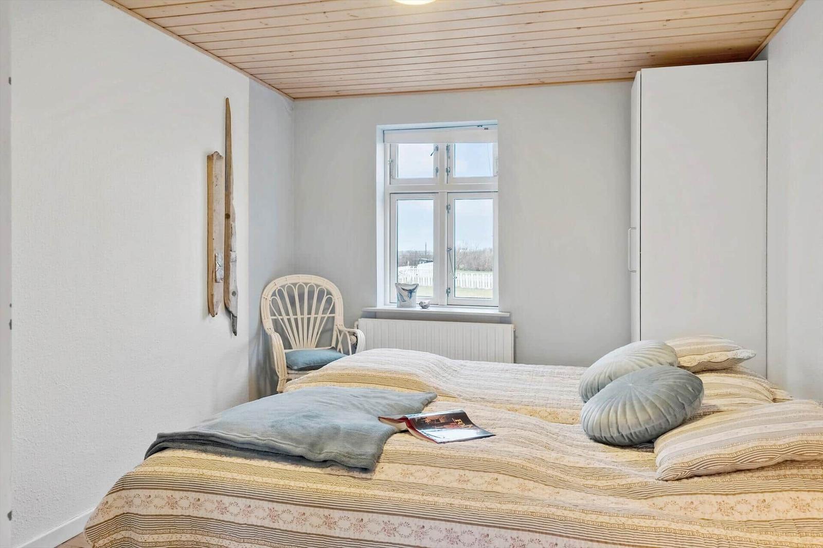 Schlafzimmer mit Bett, Stuhl und Fenster. Holzdecke und Kleidung auf dem Bett.