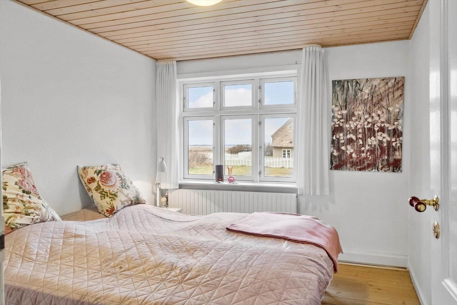 Schlafzimmer mit Bett, Fenster und Holzdecke.