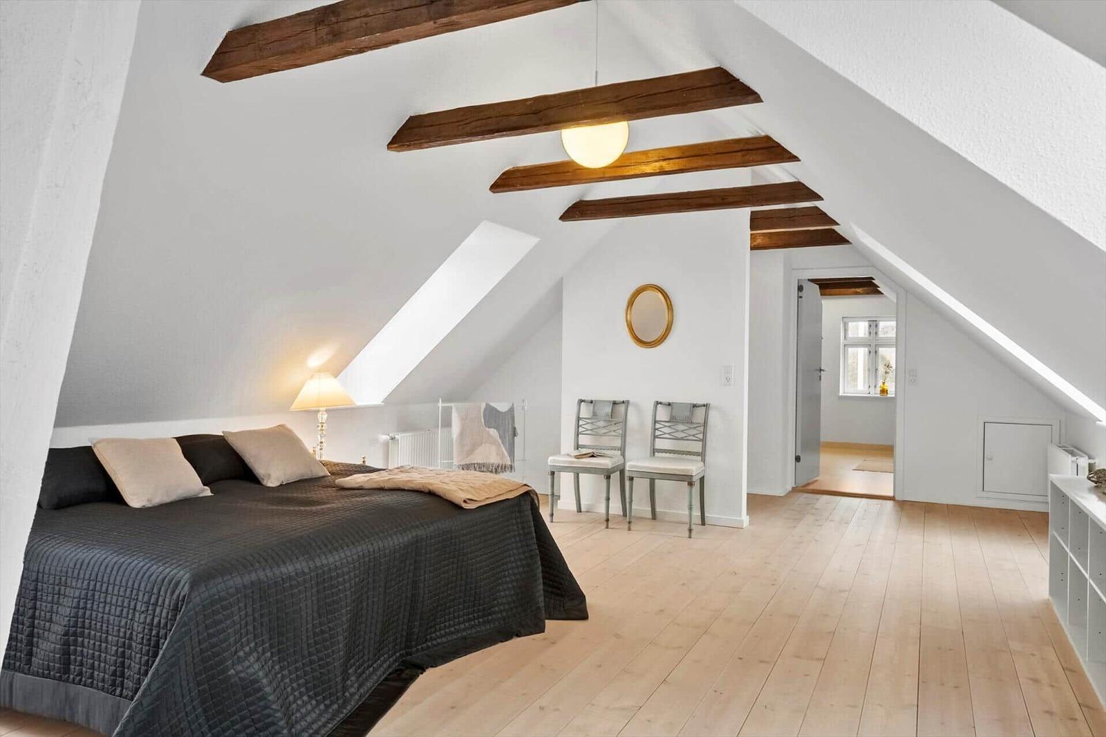 Schlafzimmer mit Dachschrägen, Holzbalken und hellem Holzboden.