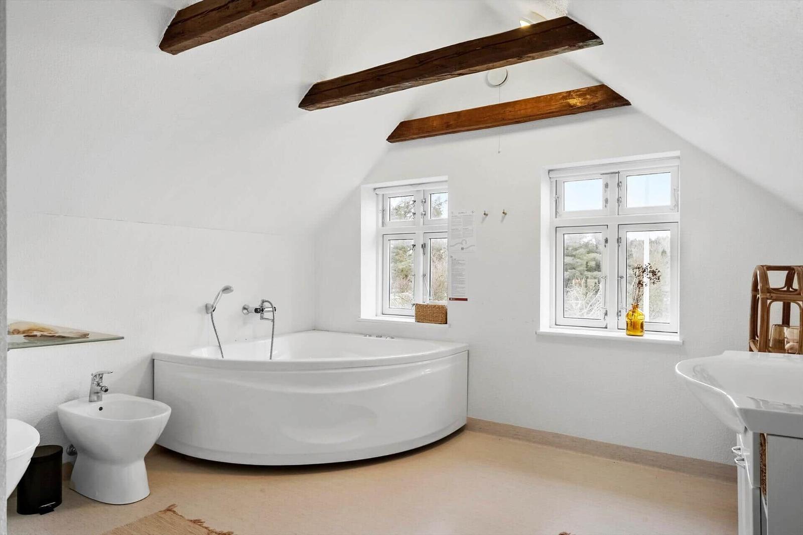 Badezimmer mit Badewanne, Fenstern und Holzbalken an der Decke.