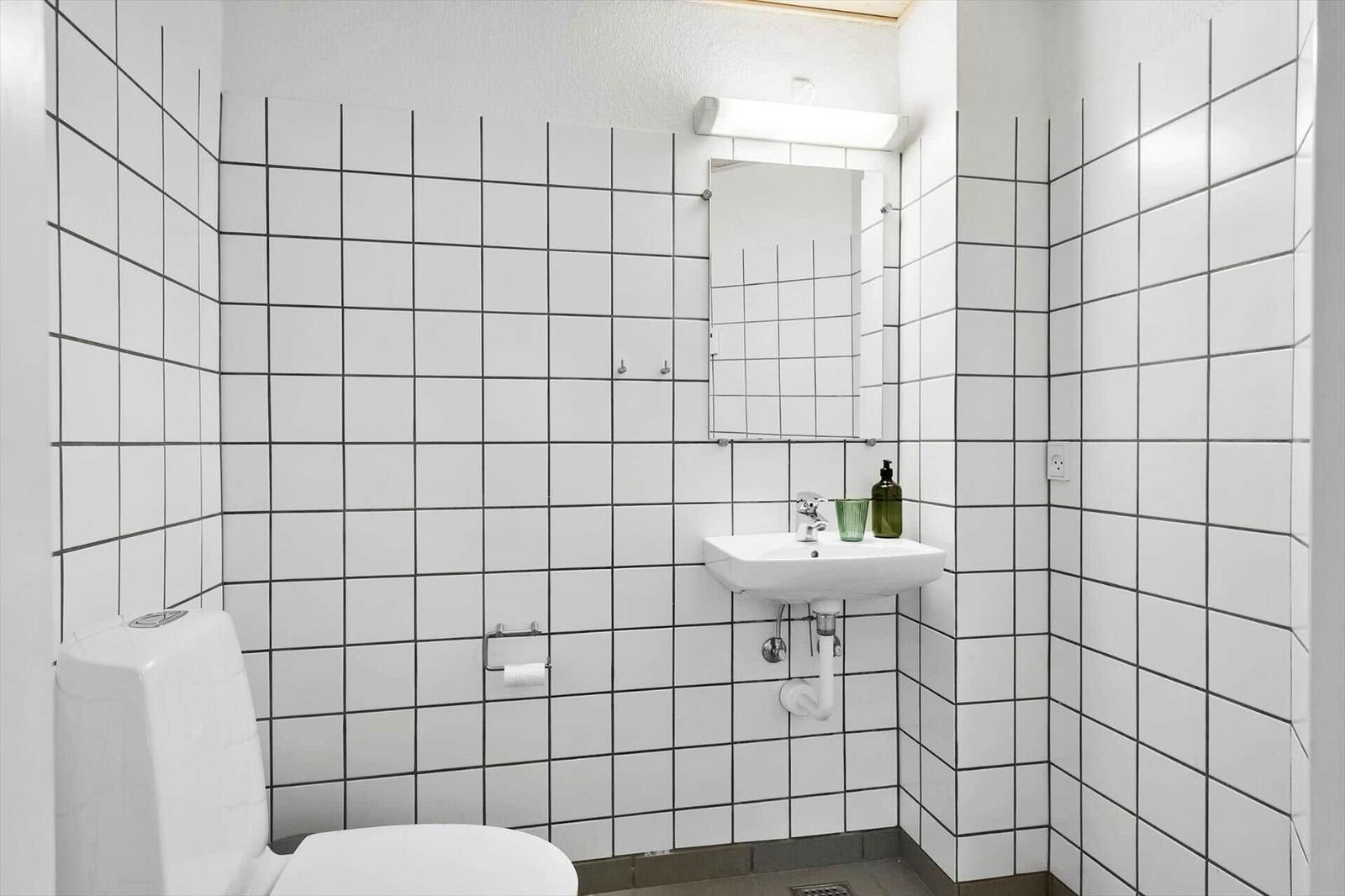 Badezimmer mit Toilette, Waschbecken und Spiegel an weißen Fliesenwänden.