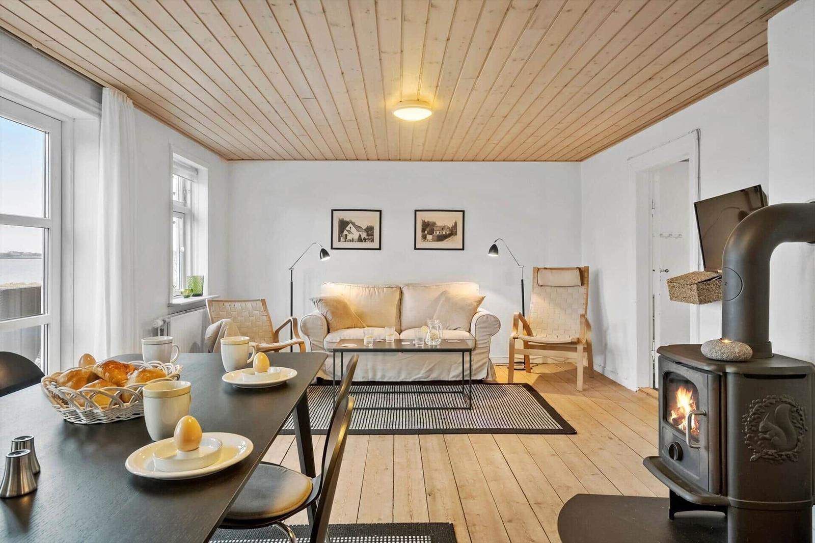 Wohnraum mit Esstisch, Sofa, Kaminofen und Holzdecke.