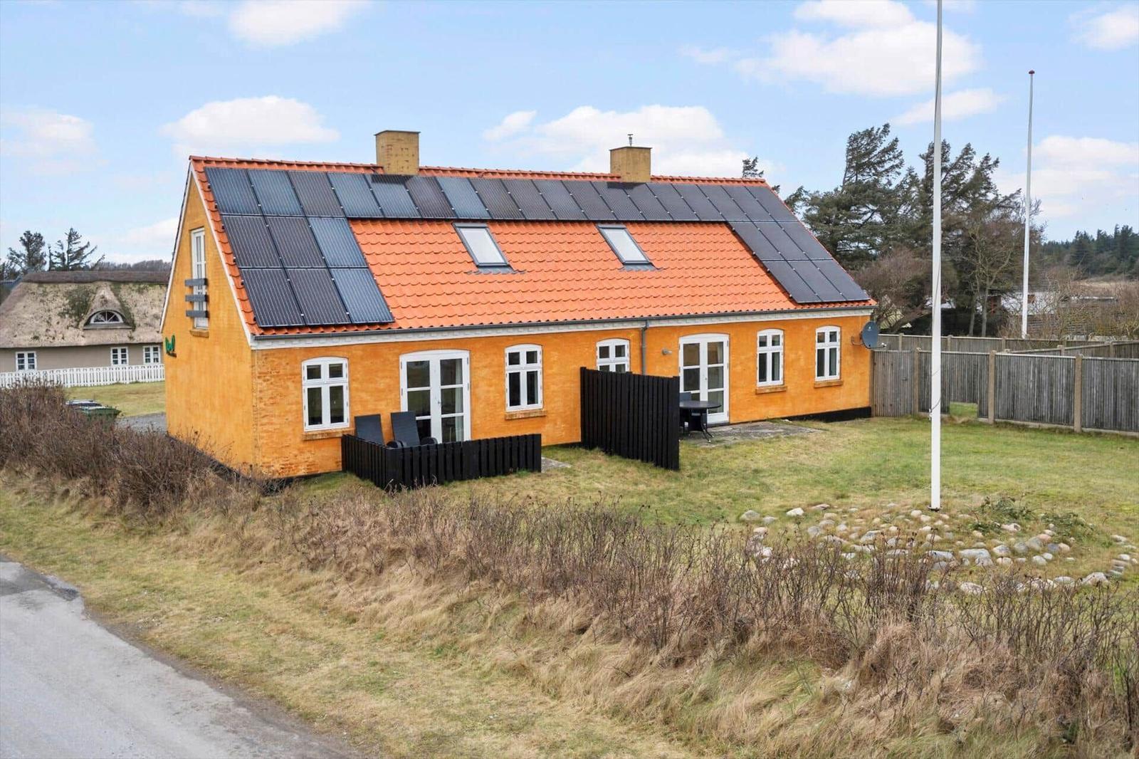 Ein gelbes Haus mit Solarpanelen auf dem Dach und einem Garten.