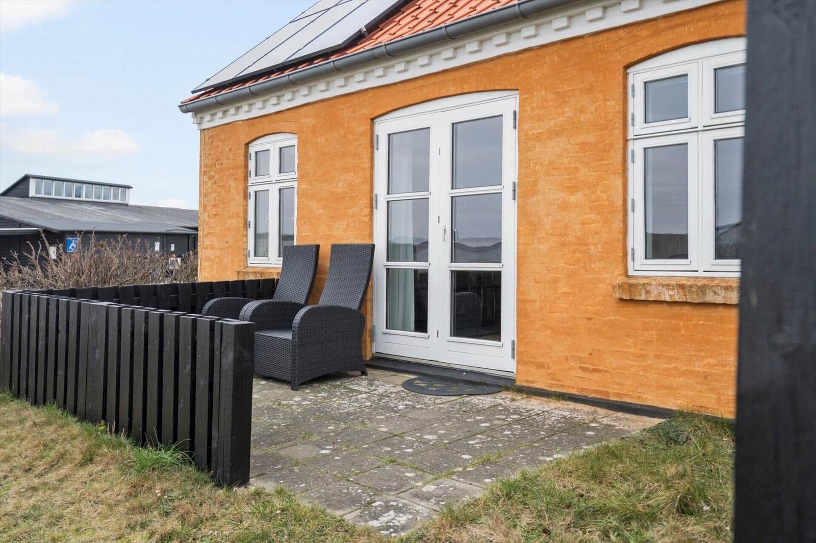 Orange Haus mit Terrasse, zwei Stühlen und Solaranlage auf Dach.