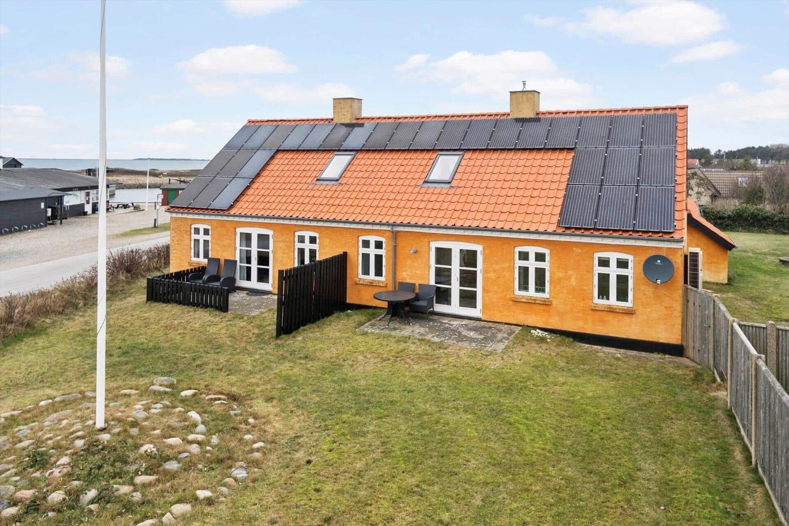 Ein gelbes Haus mit Solaranlage und Garten. Terrasse mit Tisch und Stühlen.