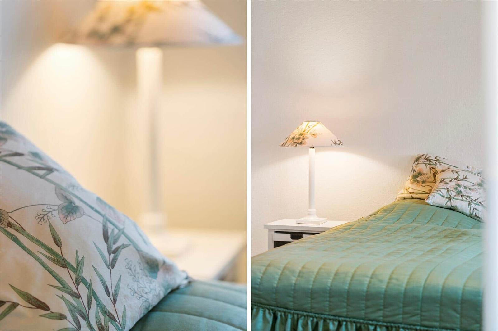 Schlafzimmer mit Bett, Nachttisch und Stehlampe mit floraler Schirmabdeckung.
