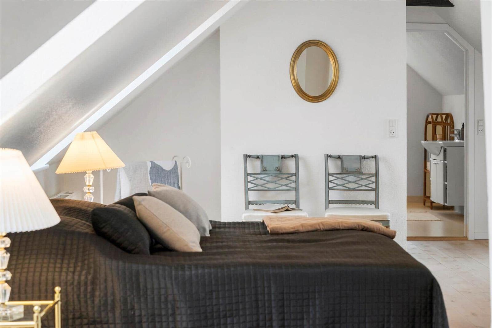 Schlafzimmer mit Dachschrägen, Bett, zwei Stühlen und Spiegel an der Wand.