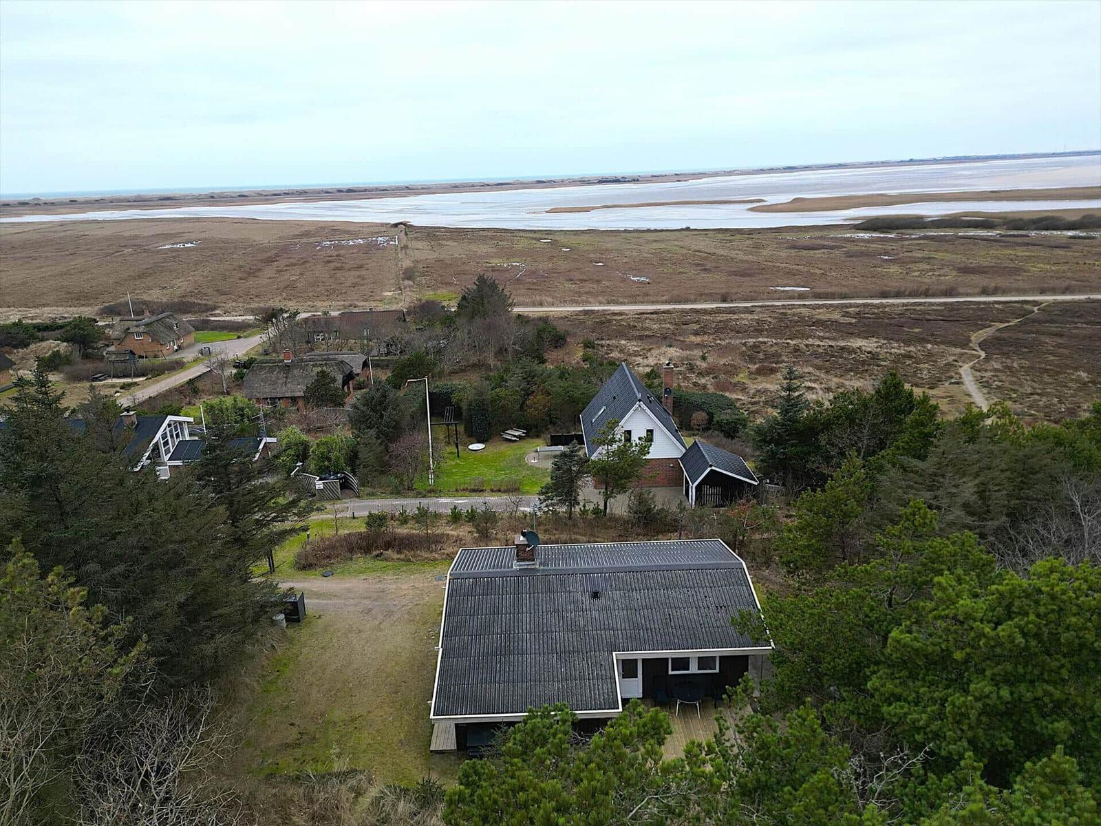 Haus mit Terrasse, umgeben von Bäumen und Blick auf Fluss und Strand.