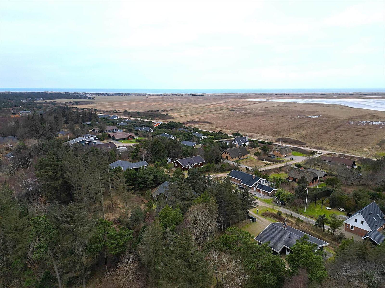Luftbild einer Siedlung mit Häusern, Wäldern und Blick auf die Küste.