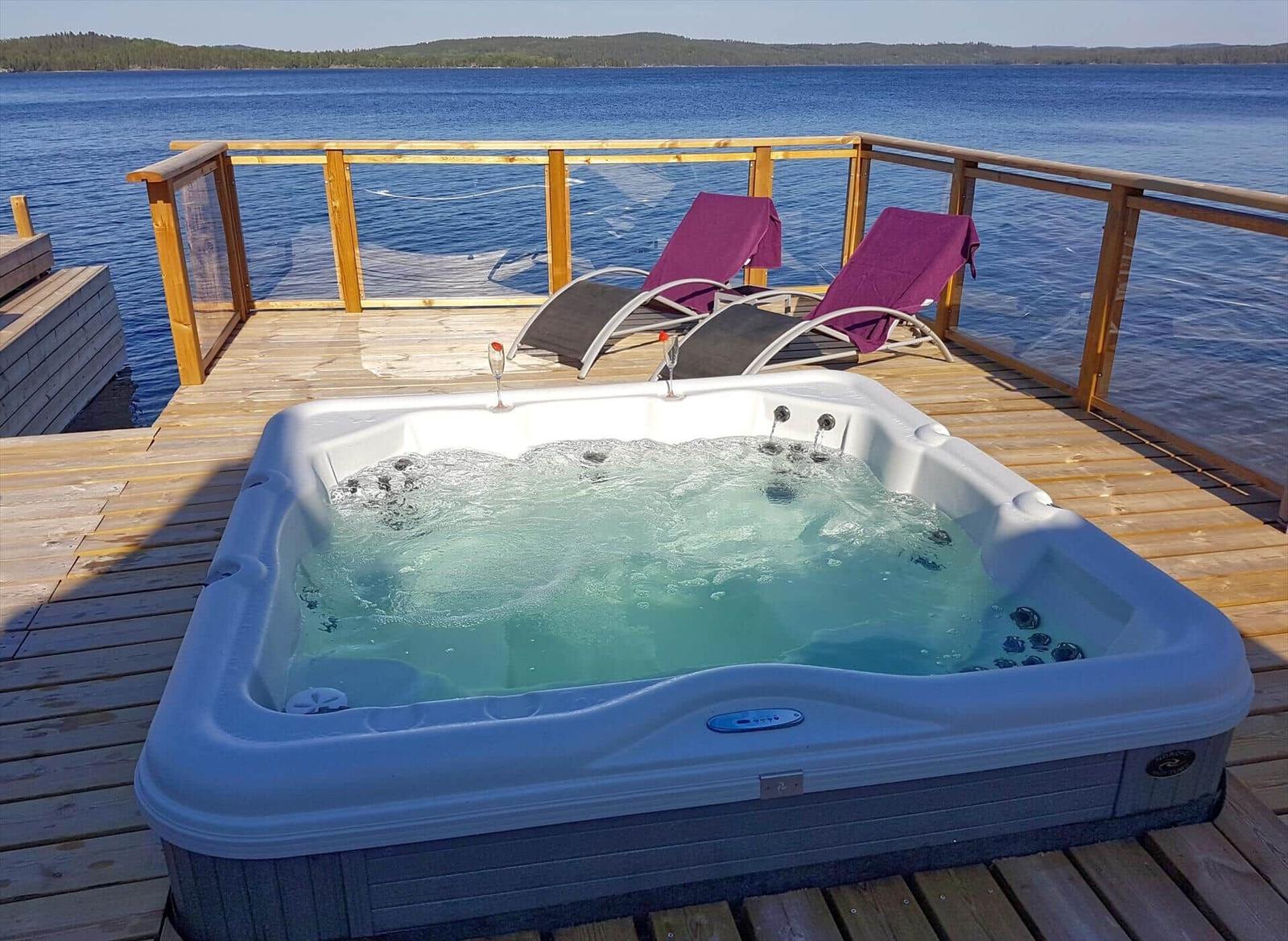 Whirlpool auf Terrasse mit Blick auf See und zwei Liegestühle mit lila Decken.