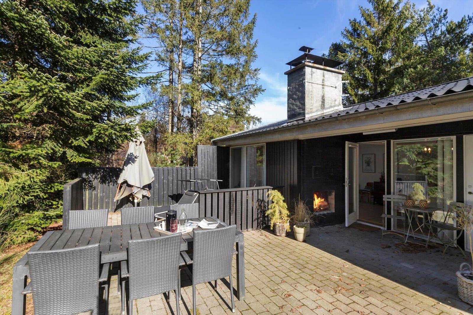 Terrace with seating area, grill space, and wooden house with fireplace and windows.