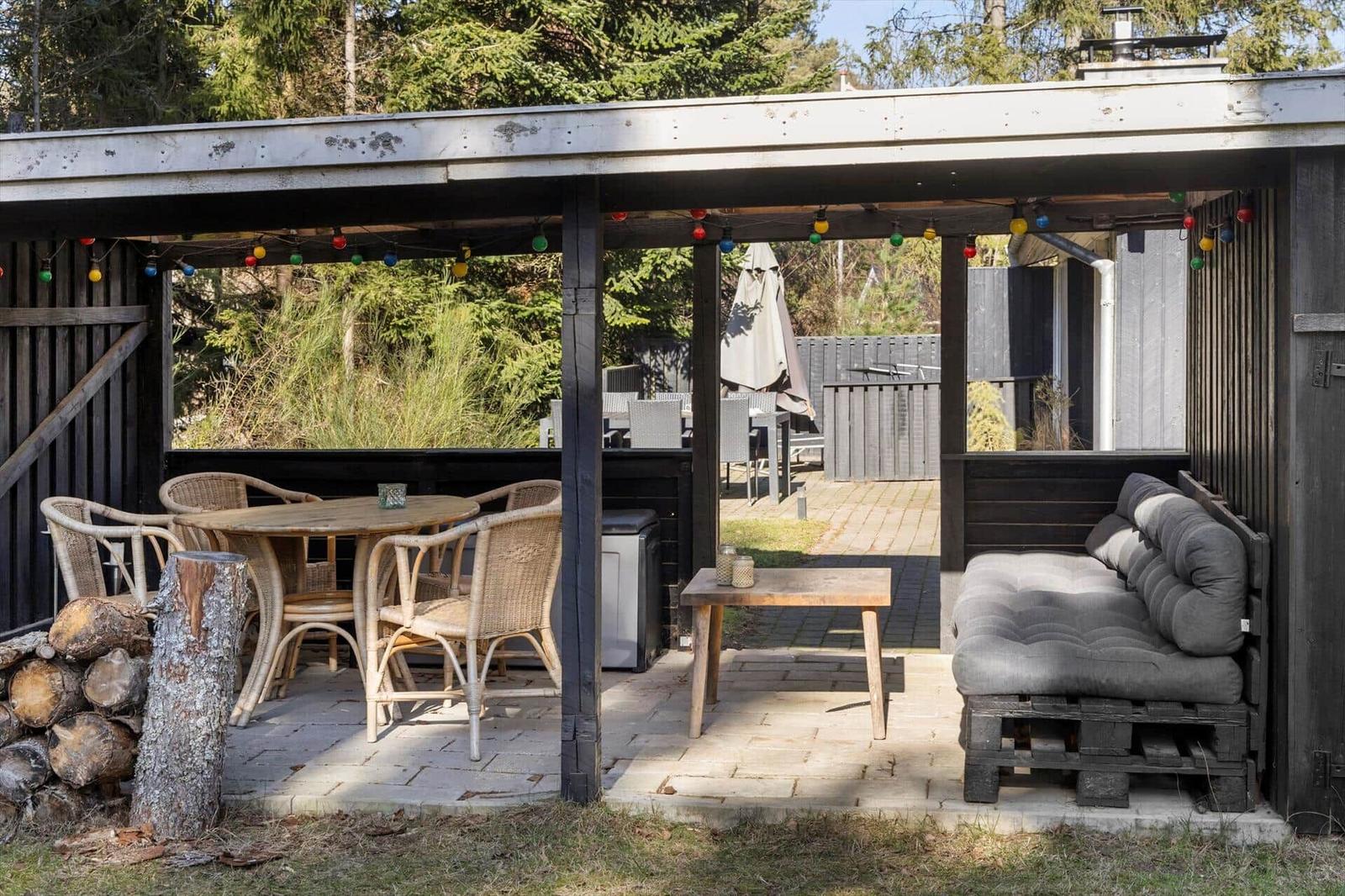 Terrace with table, chairs, and sofa under a roof with string lights.