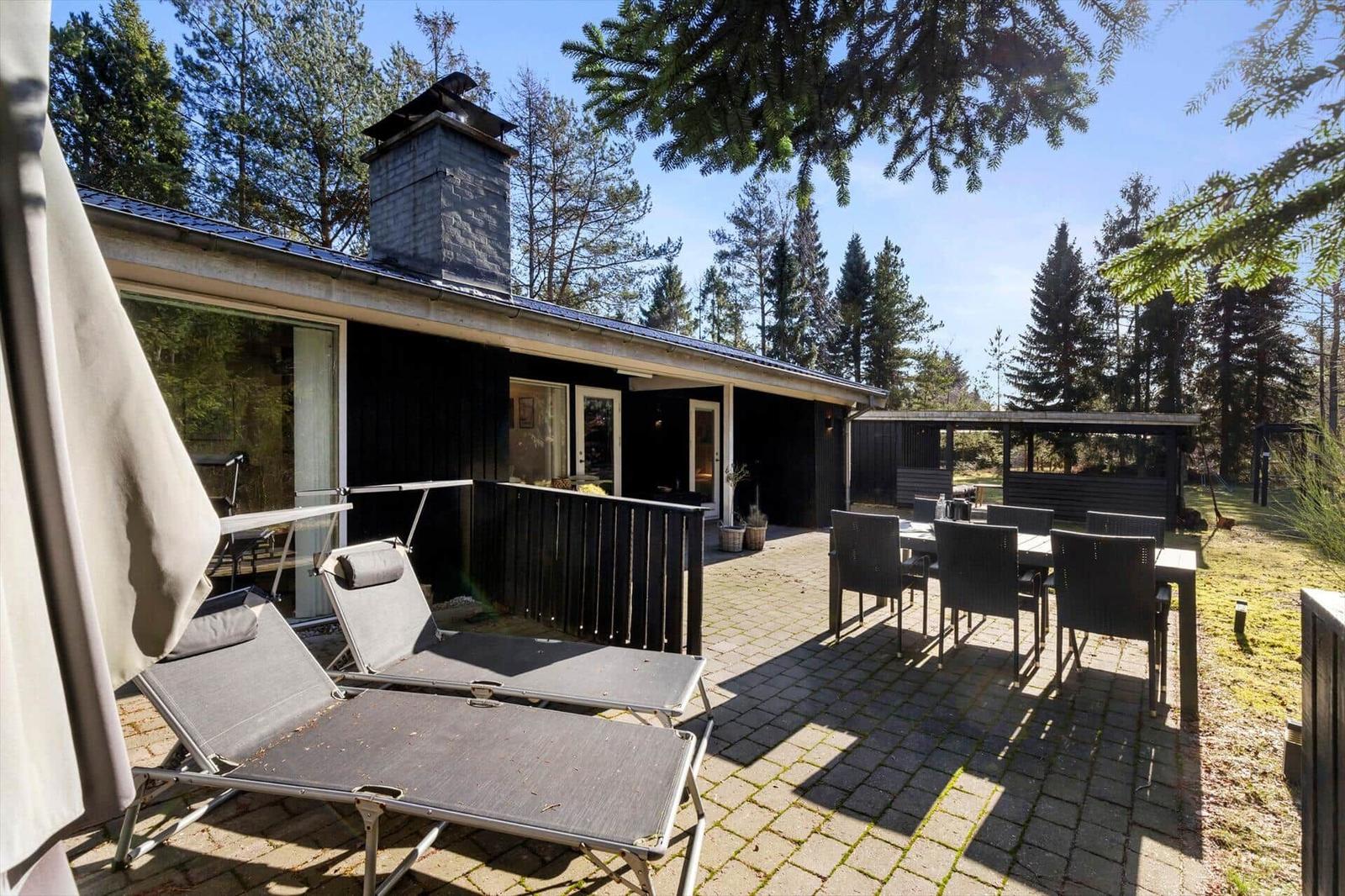 Modern wooden cabin with terrace, lounge chairs, and table in the woods.