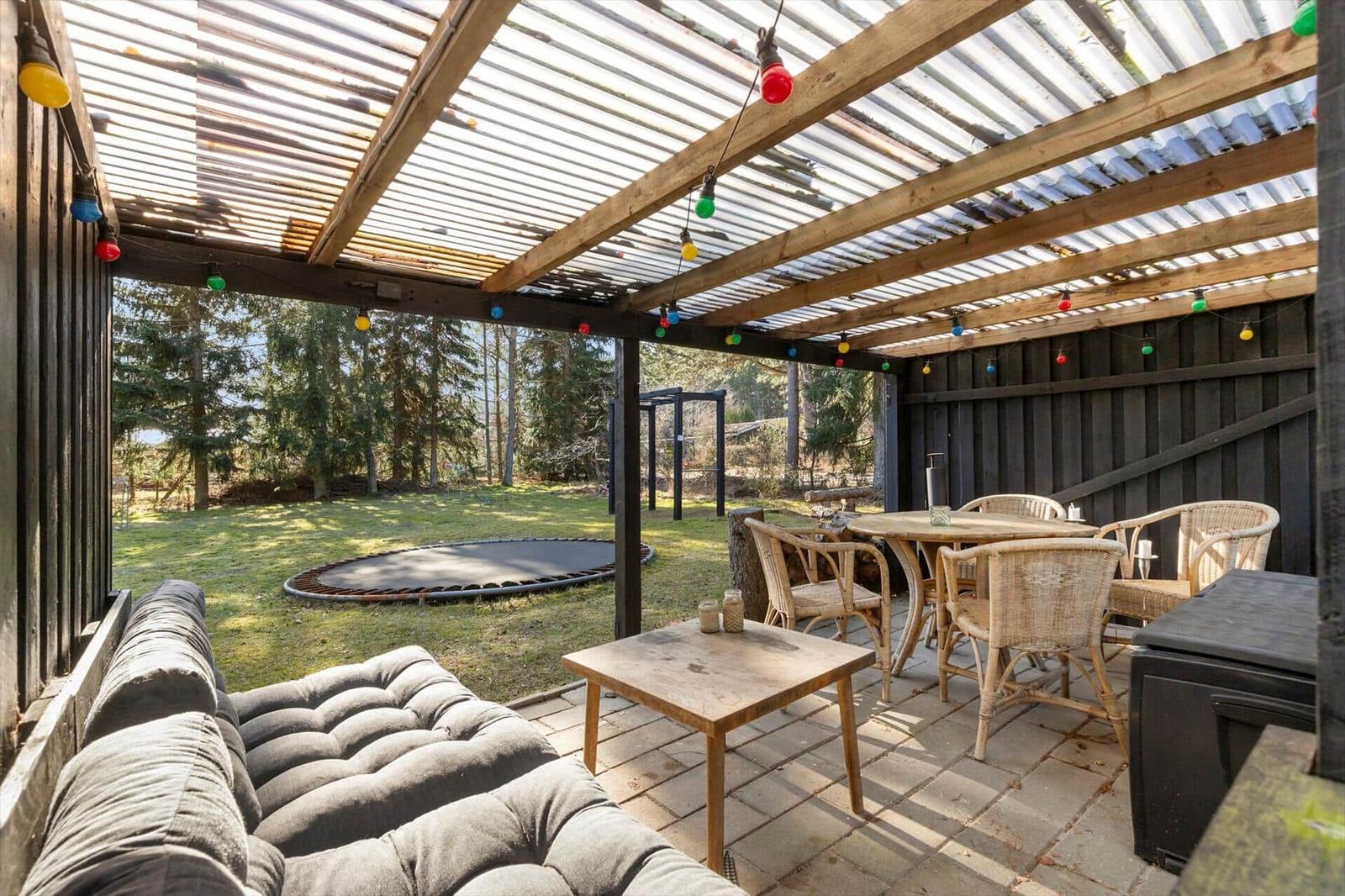 Terrace with seating, table, trampoline, and wood cladding.