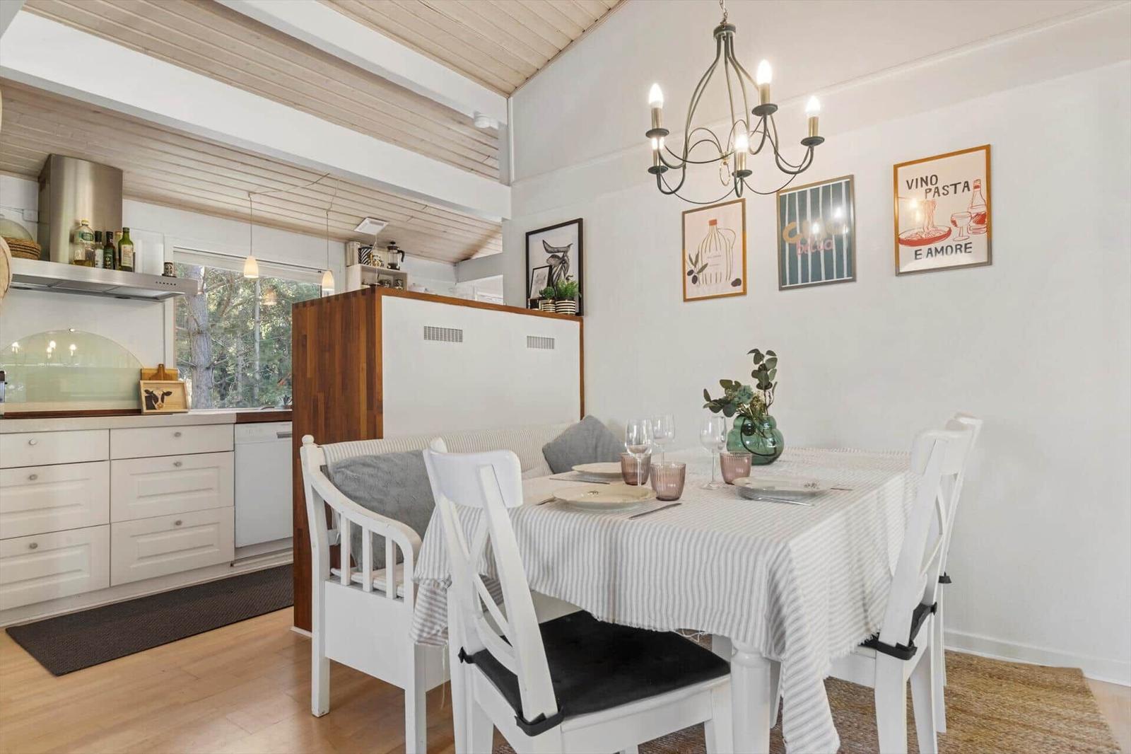 Dining room with table, chairs, and kitchen area. Wall decor and chandelier.