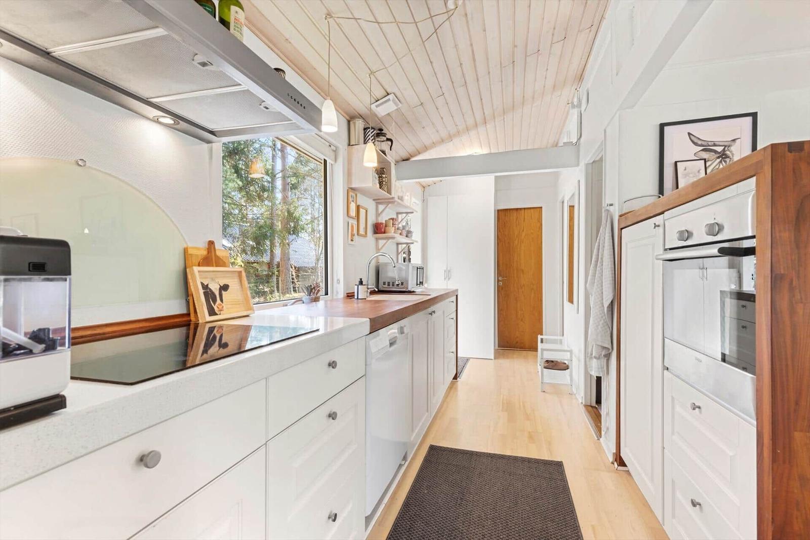 Kitchen with wooden floor, white cabinets, and wooden tools. Window view of forest.
