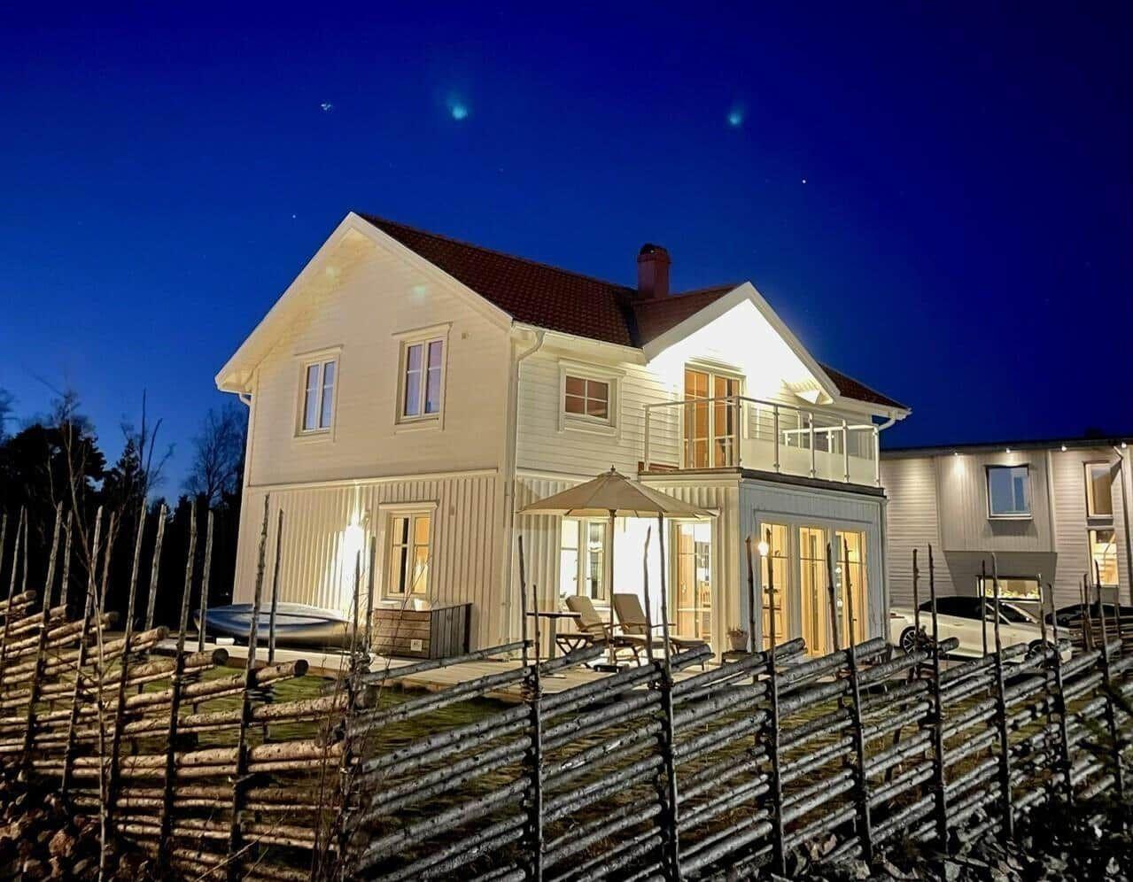 Haus mit beleuchteten Fenstern und Terrasse unter sternenklarem Himmel.