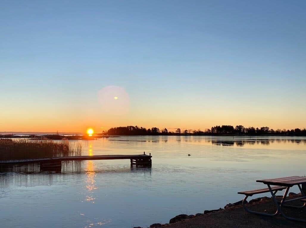 Sonnenuntergang über ruhigem See mit Steg und Picknicktisch