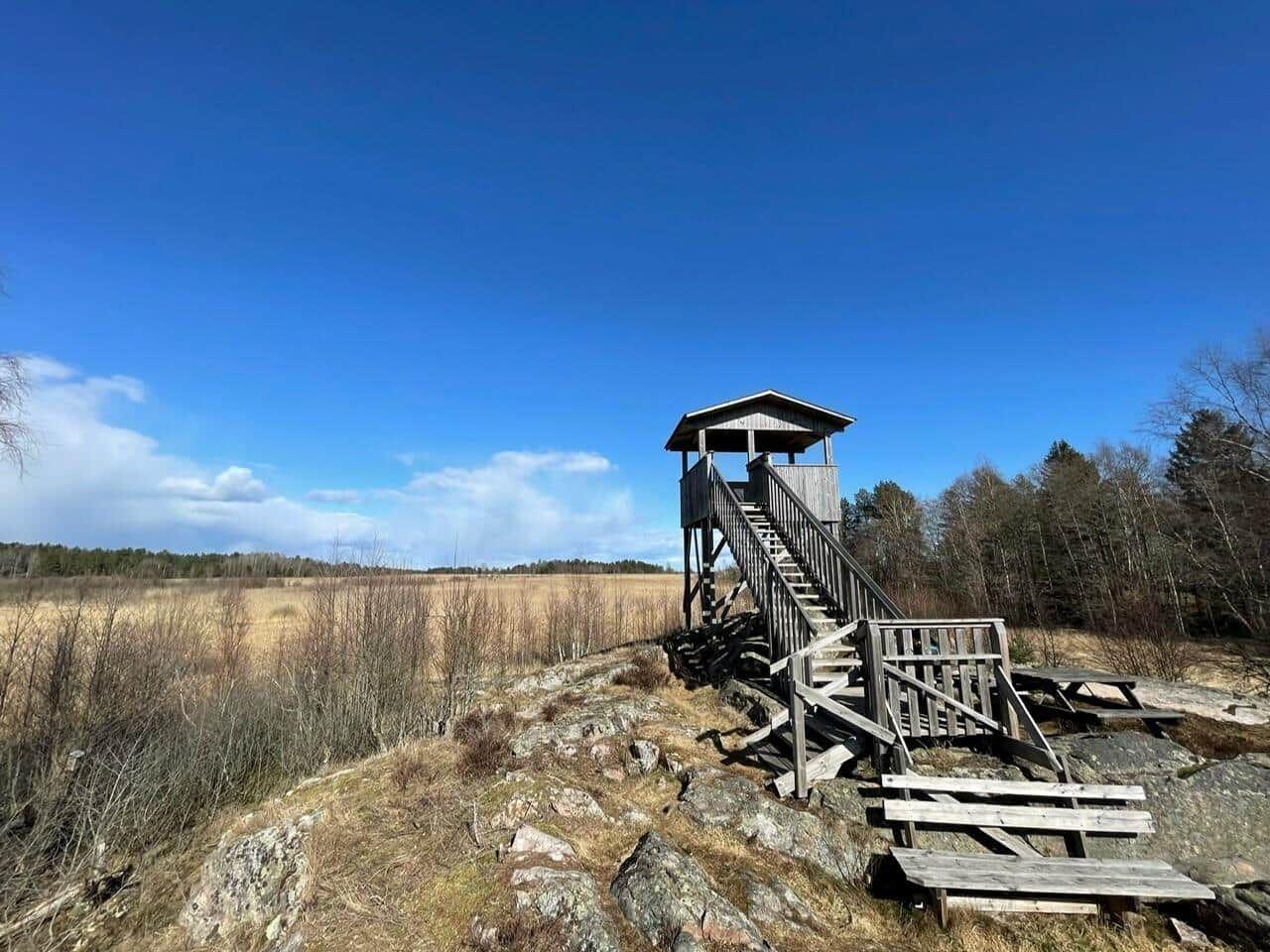Holzbeobachtungsturm auf felsigem Hügel mit Blick auf Wald und Feld.